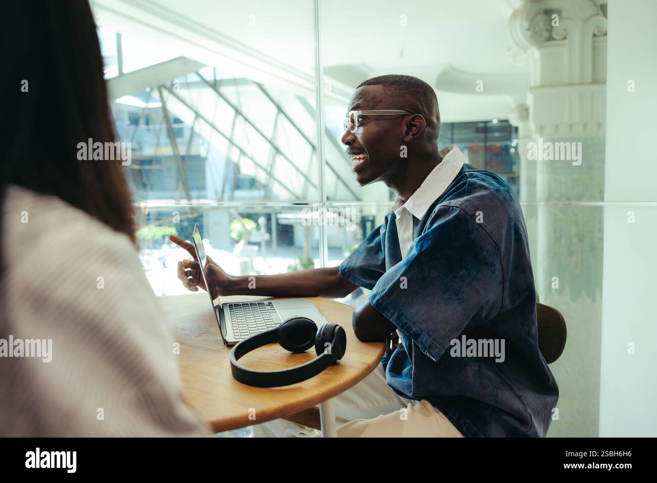 Un étudiant masculin est assis dans un cadre universitaire urbain, conversant activement tout en travaillant sur un ordinateur portable, représentant l'éducation et la communication modernes. Banque D'Images