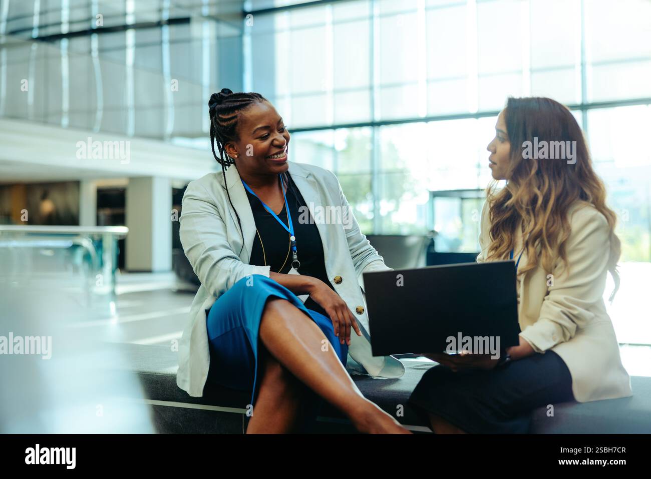 Deux collègues professionnelles s'engagent dans la conversation tout en étant assis dans un hall lumineux et moderne. Ils partagent des idées et travaillent sur un ordinateur portable, refl Banque D'Images