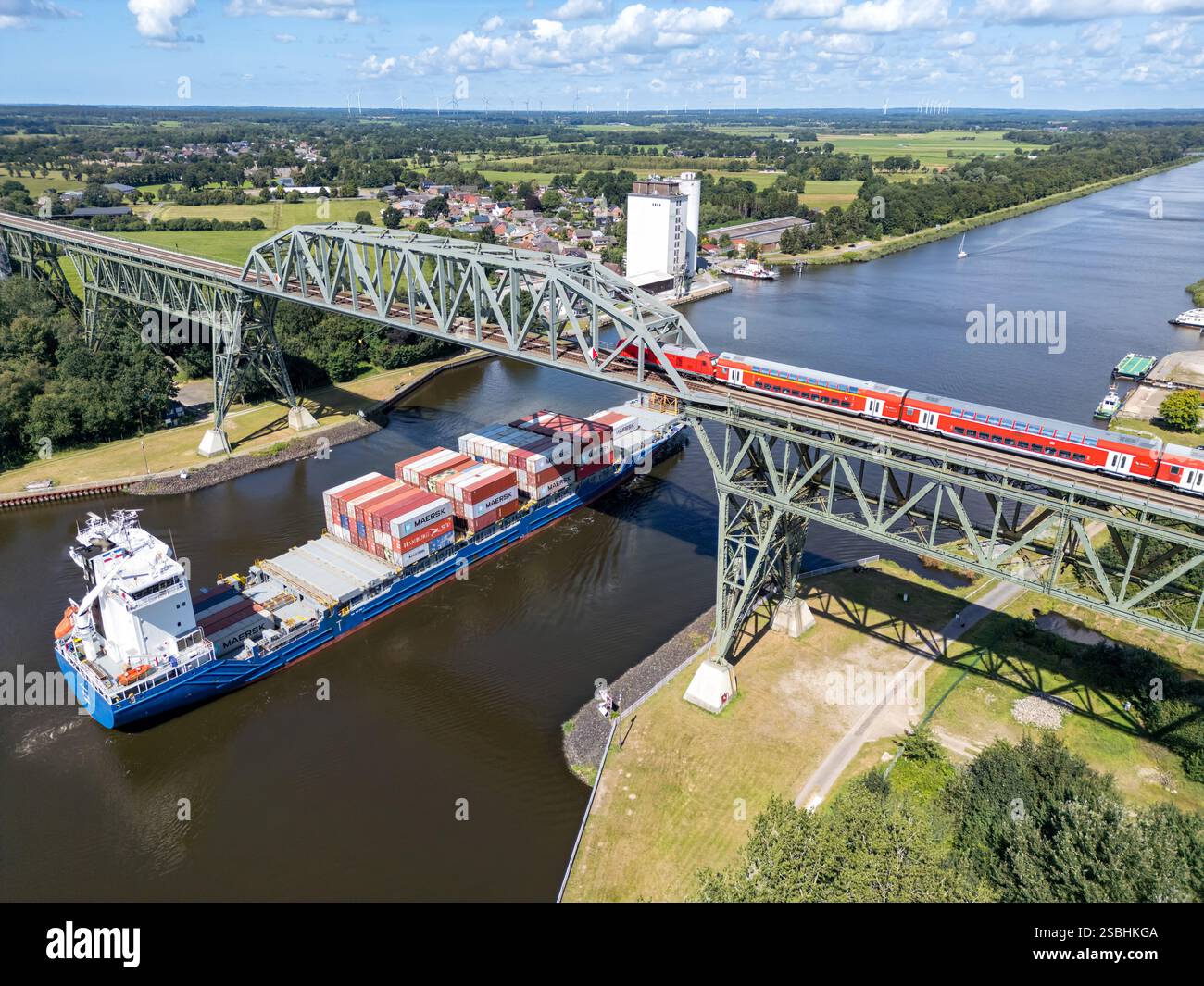 Hochdonn, Allemagne - 12 août 2024 : vue aérienne du haut pont de Hochdonn traversant le canal de Kiel avec un train régional et un porte-conteneurs à Hochdon Banque D'Images