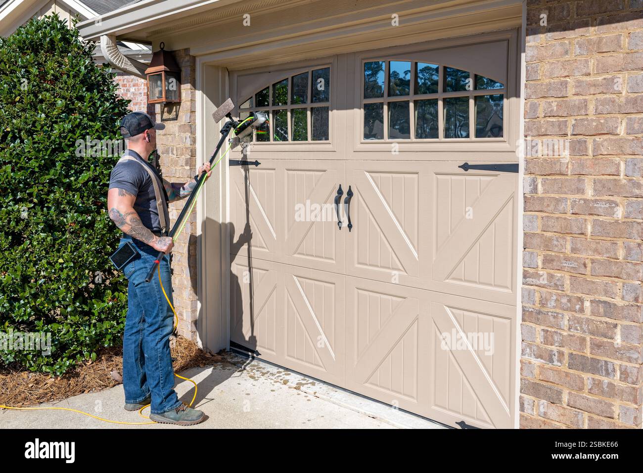 Homme adulte lave-vitre employé ou travailleur lavant les fenêtres sur une maison résidentielle ou une maison en Amérique de banlieue en Alabama USA. Banque D'Images