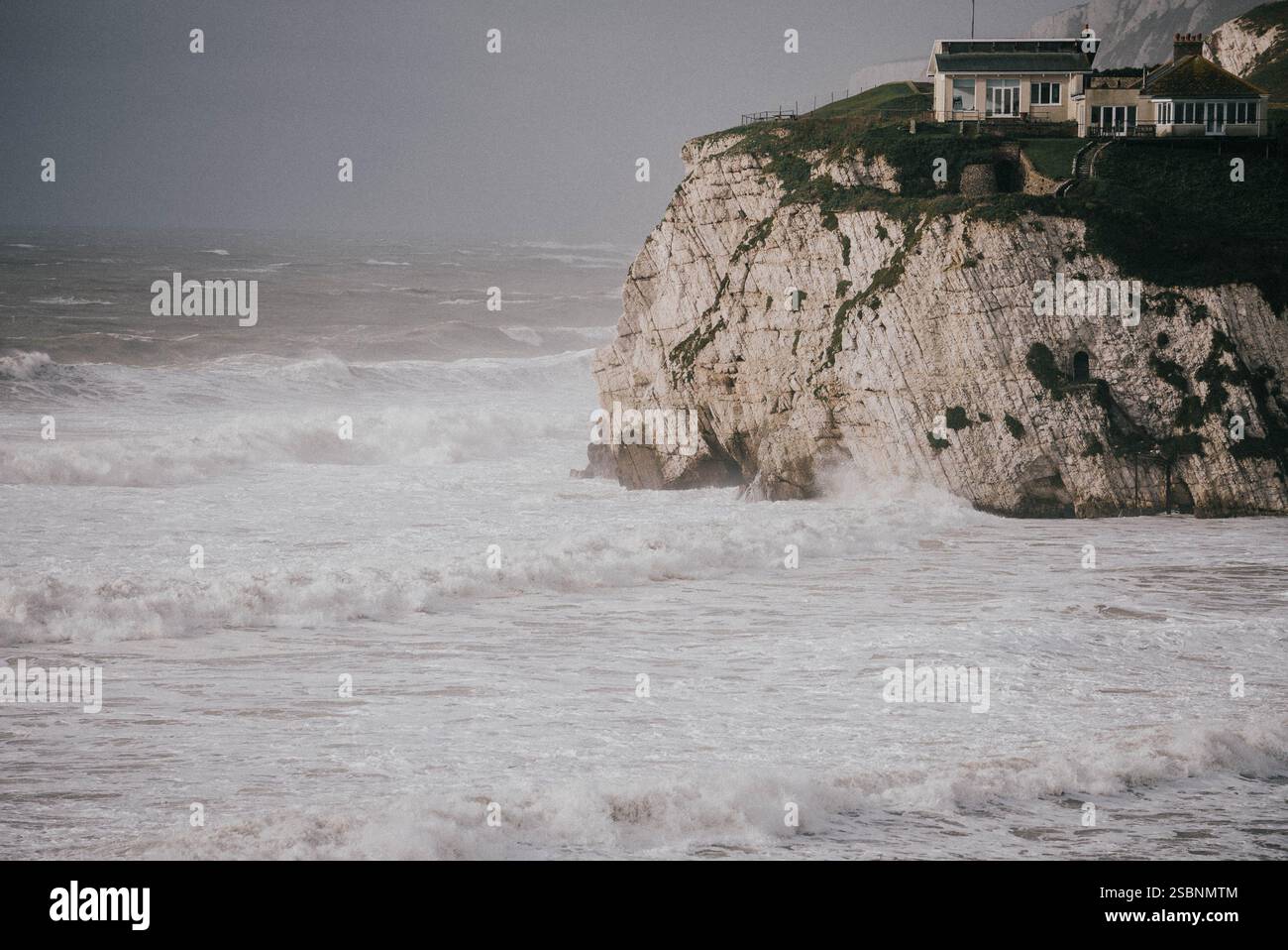 Une maison est sur une falaise surplombant l'océan. Les vagues s'écrasent contre les rochers et le ciel est nuageux Banque D'Images