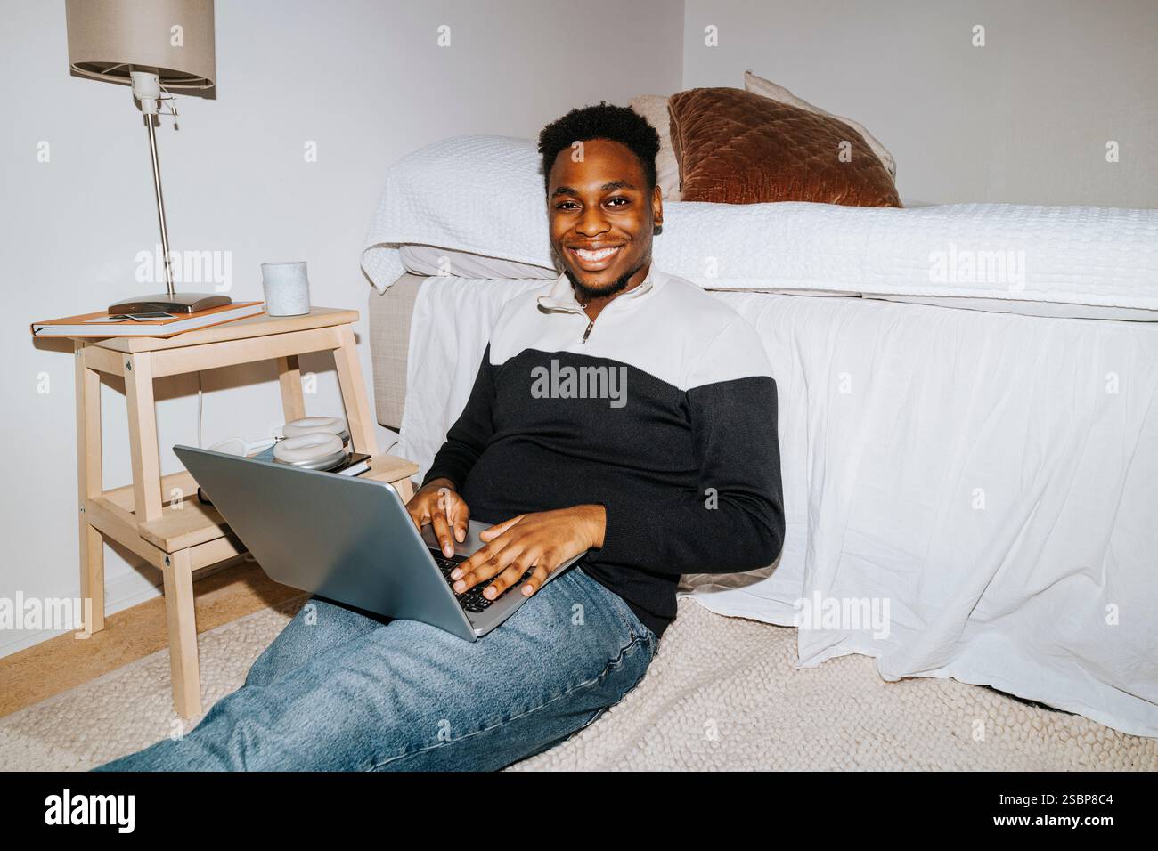 Portrait d'étudiant masculin souriant avec ordinateur portable assis par le lit dans la chambre de dortoir Banque D'Images