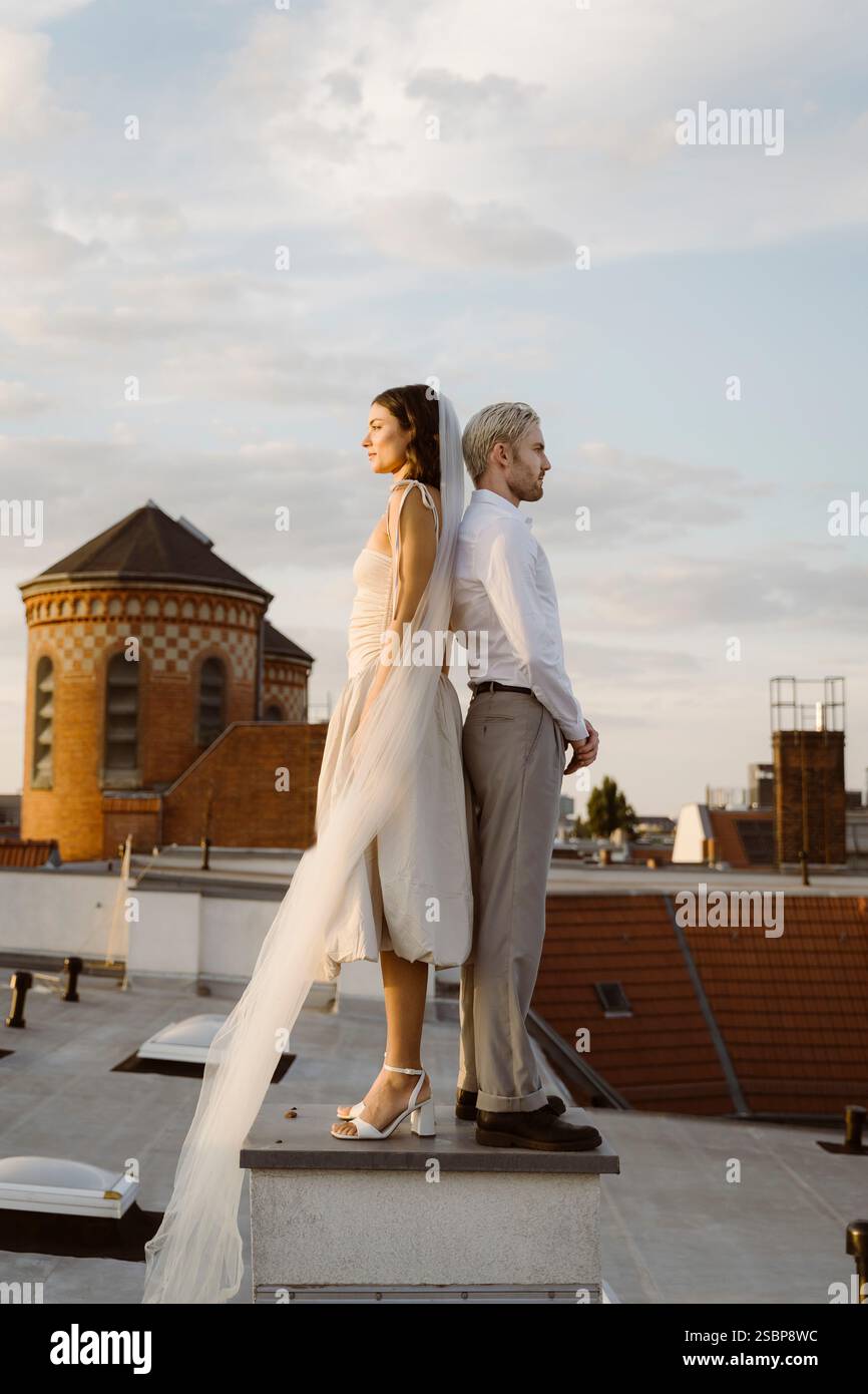 Vue latérale du jeune pont et du marié debout dos à dos sur le toit Banque D'Images