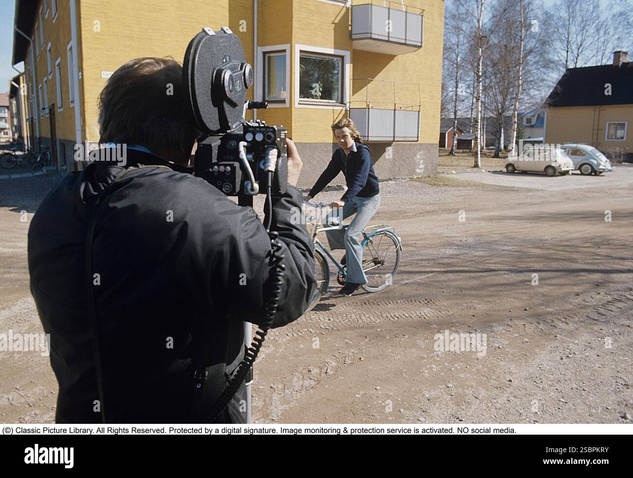 Tournage dans les années 1970 L'acteur chanteur Björn Skifs est vu à vélo en passant devant le directeur de la photographie avec sa caméra sur son épaule. Banque D'Images