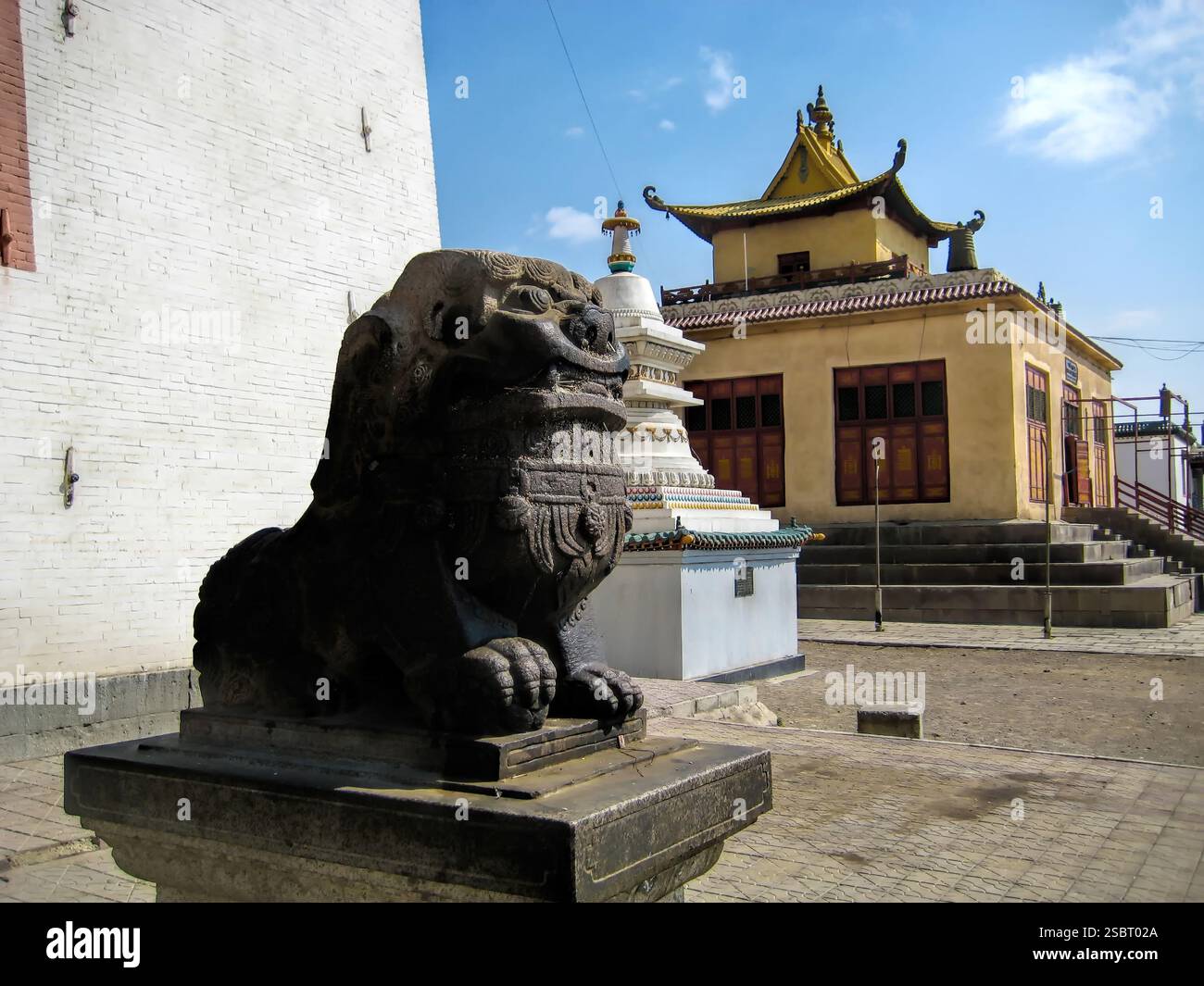 Une grande statue noire d'un dragon est assise sur une base de pierre. La statue se trouve devant un bâtiment au toit jaune Banque D'Images