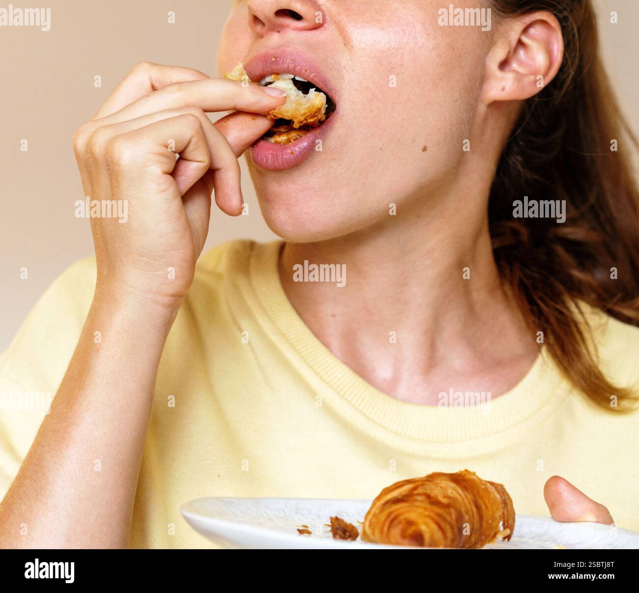 Concept de suralimentation et de bouffée de nourriture. Jeune femme affamée mangeant un croissant Banque D'Images