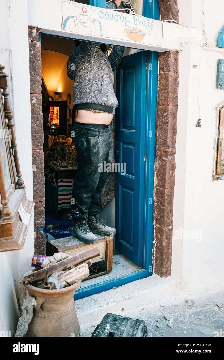 Un artisan se tient dans la porte d'un magasin d'une vieille radio en réparation, Oia, Santorin, Grèce Banque D'Images