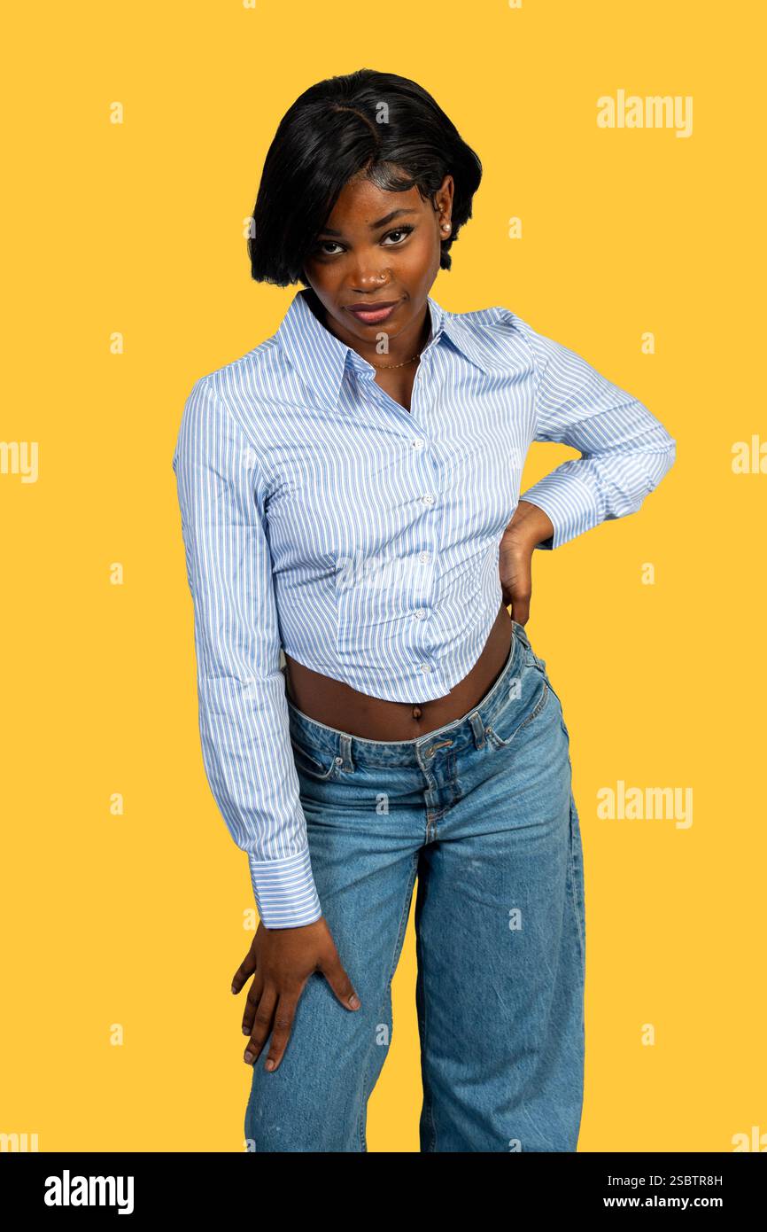 Portrait studio d'une jeune femme noire élégante posant avec confiance sur un fond jaune vif Banque D'Images