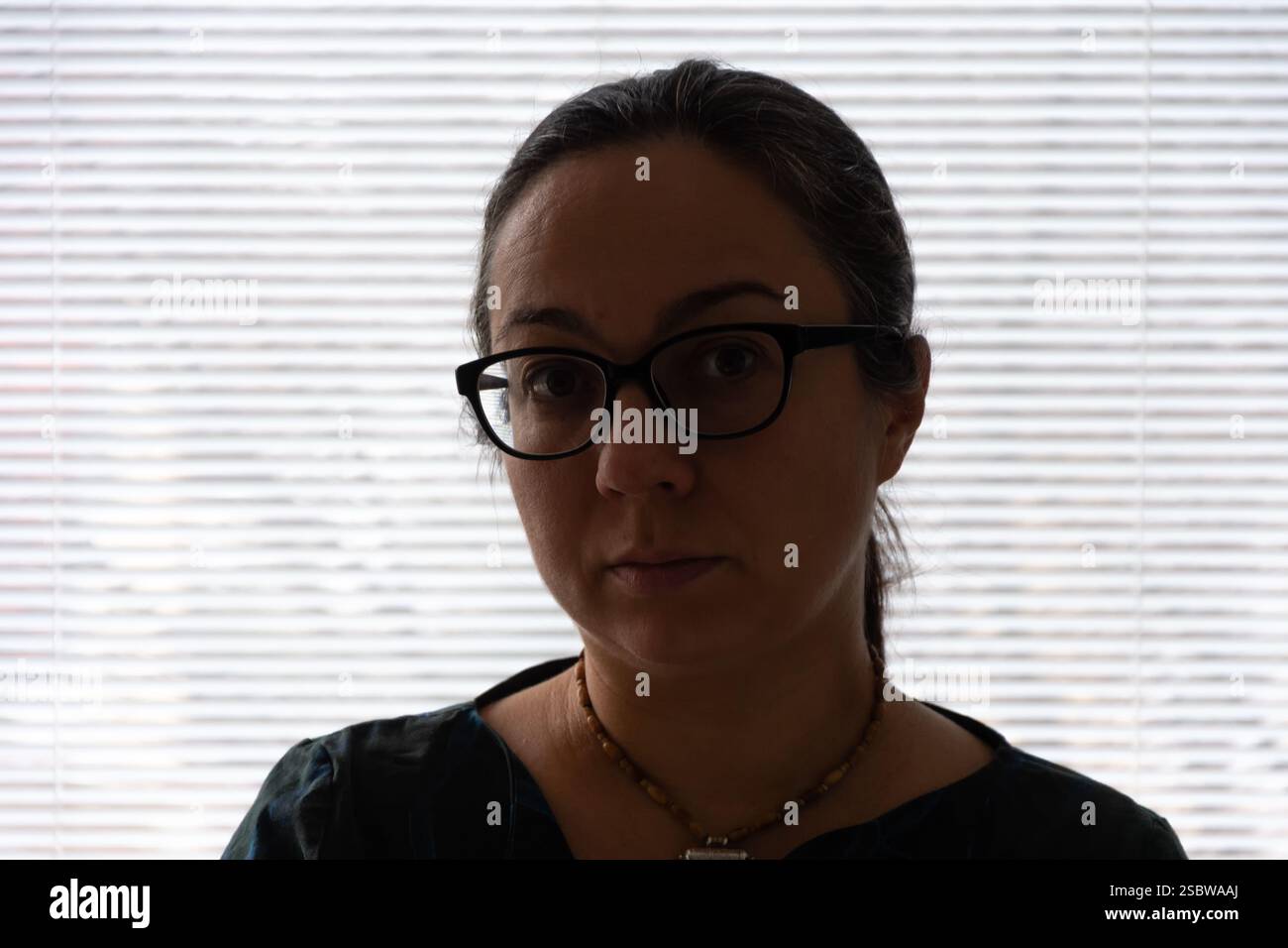 Une femme portant des lunettes pose contre une fenêtre lumineuse, silhouettée en contre-jour Banque D'Images
