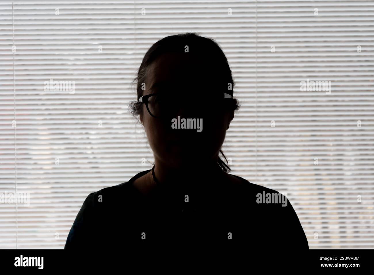 Portrait d'une femme au visage sombre contre une fenêtre de lumière du jour Banque D'Images