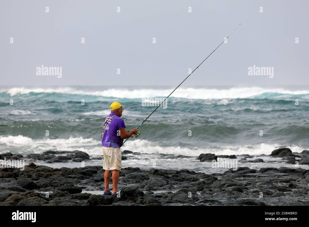 Homme mûr solitaire pêchant avec canne à pêche sur le rivage volcanique rocheux, Fuerteventura, îles Canaries, Espagne. Prise en novembre 2024 Banque D'Images