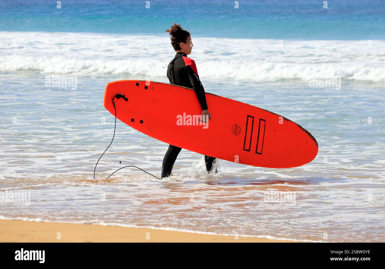 Femme portant une planche de surf vers la mer à Piedra Playa plage, El Cotillo, Fuerteventura, Îles Canaries, Espagne. Prise en novembre 2024 Banque D'Images