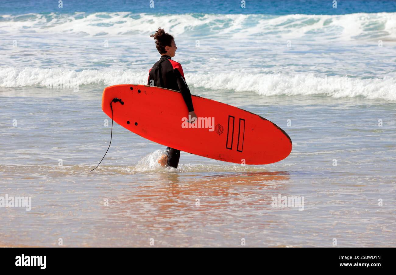 Femme portant une planche de surf vers la mer à Piedra Playa plage, El Cotillo, Fuerteventura, Îles Canaries, Espagne. Prise en novembre 2024 Banque D'Images