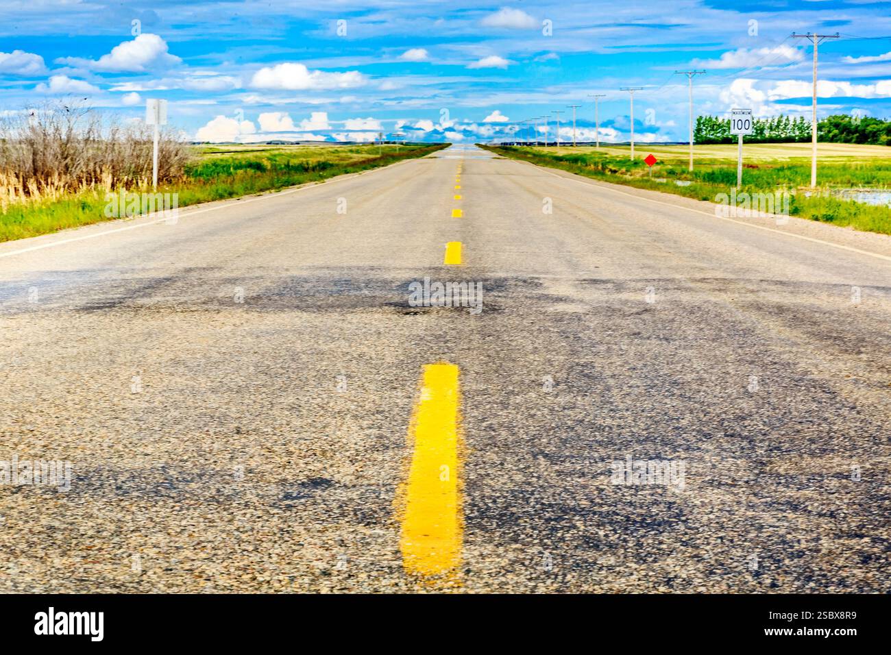 Longue route avec des lignes jaunes et pas de voitures. Il y a un panneau sur le côté de la route Banque D'Images