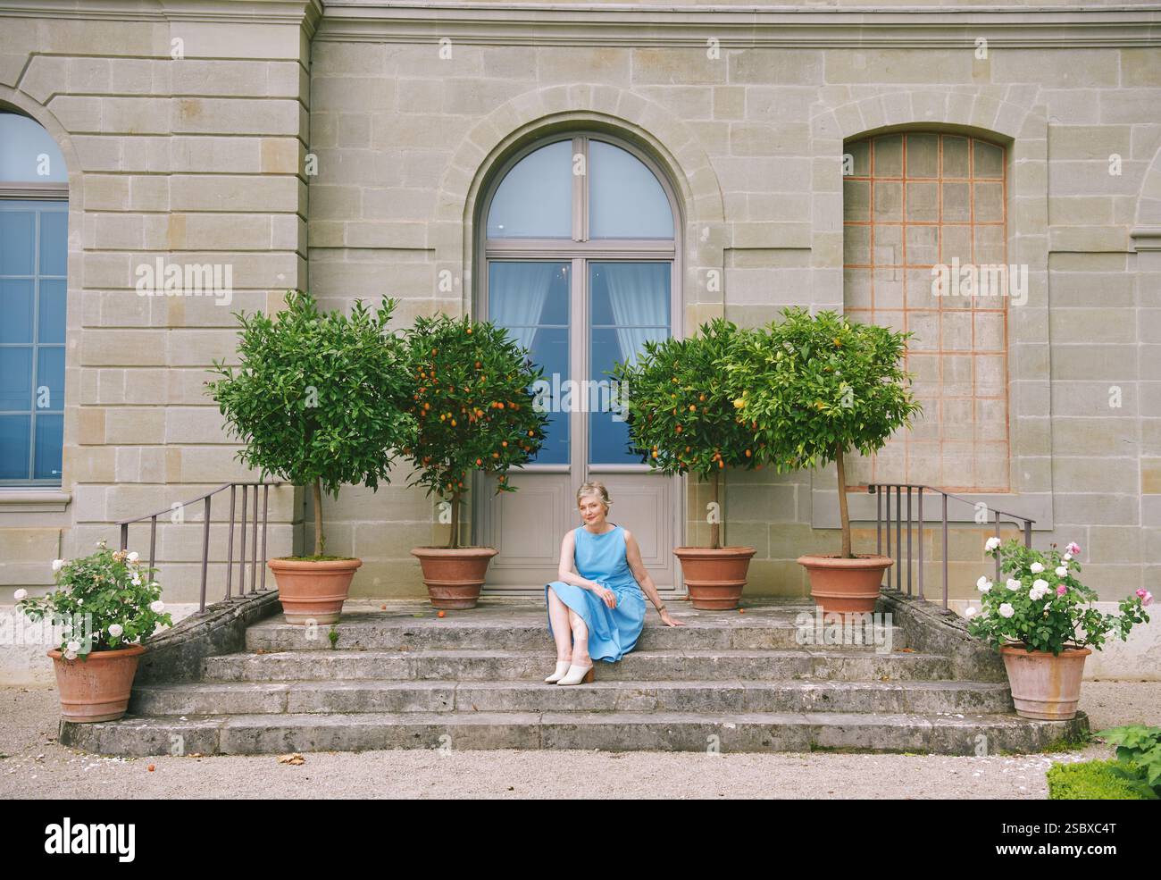 Portrait complet de la longueur du corps de belle femme d'âge moyen de 50 -55 ans, portant une robe bleue, posant dehors à côté de citronniers plantés Banque D'Images