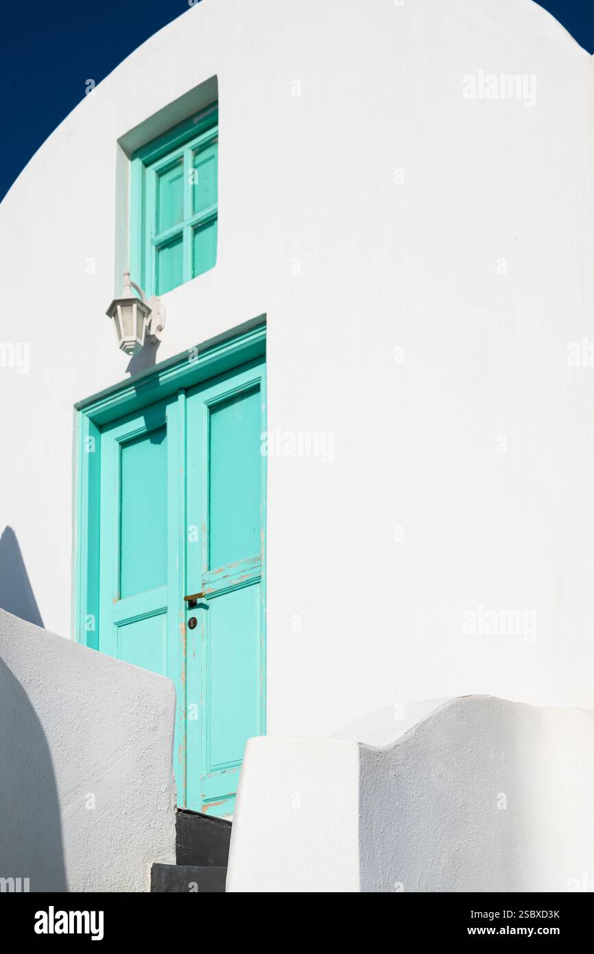 Maison blanche en forme de bloc avec toit en forme de tonneau et portes et fenêtres bleu-vert à la lumière du soleil, Oia, Santorin, Grèce Banque D'Images