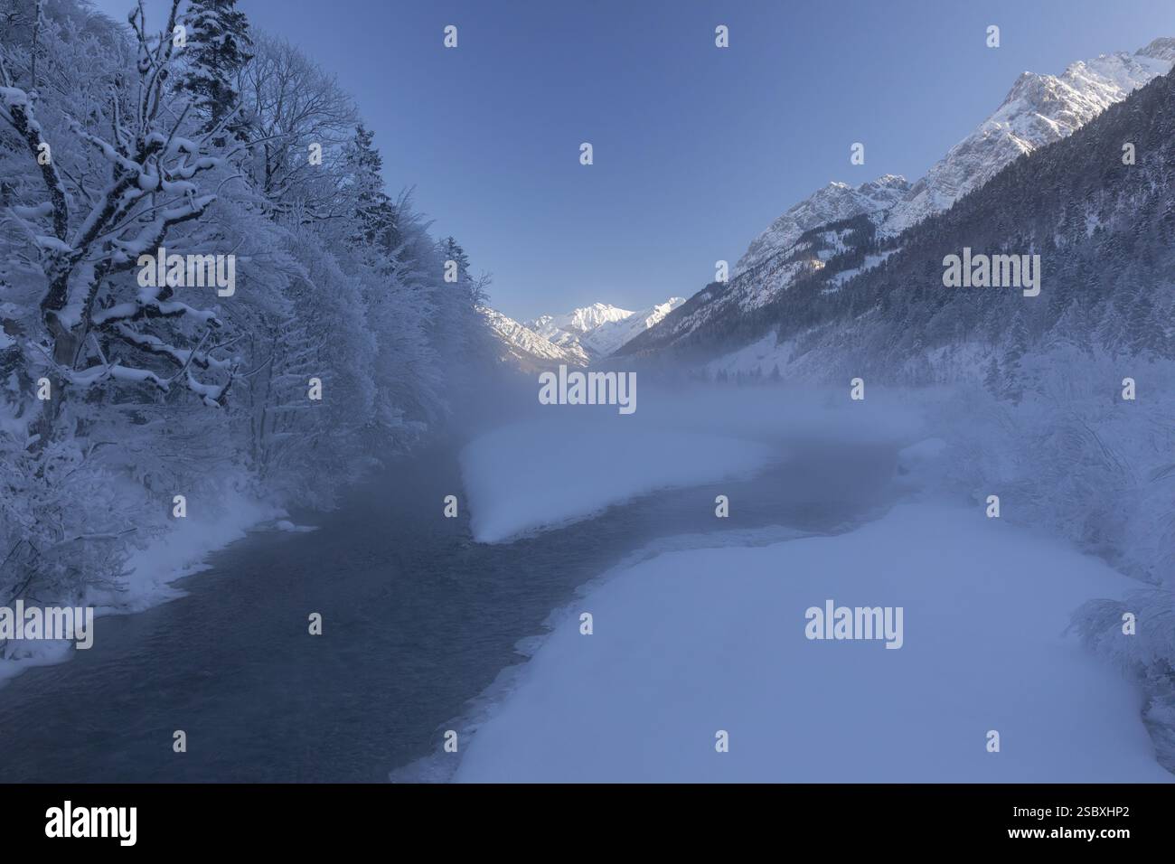 Le ruisseau Riss coulant à travers un paysage enneigé dans la vallée de l'Eng. Journée ensoleillée avec ciel bleu. Le ruisseau est dans l'ombre profonde avec un peu de brouillard sur elle wh Banque D'Images