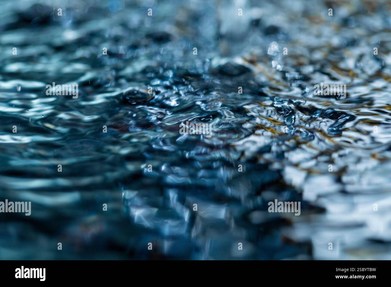 Surface irrégulière de l'eau liquide, perturbée par des gouttelettes tombant et des éclaboussures Banque D'Images