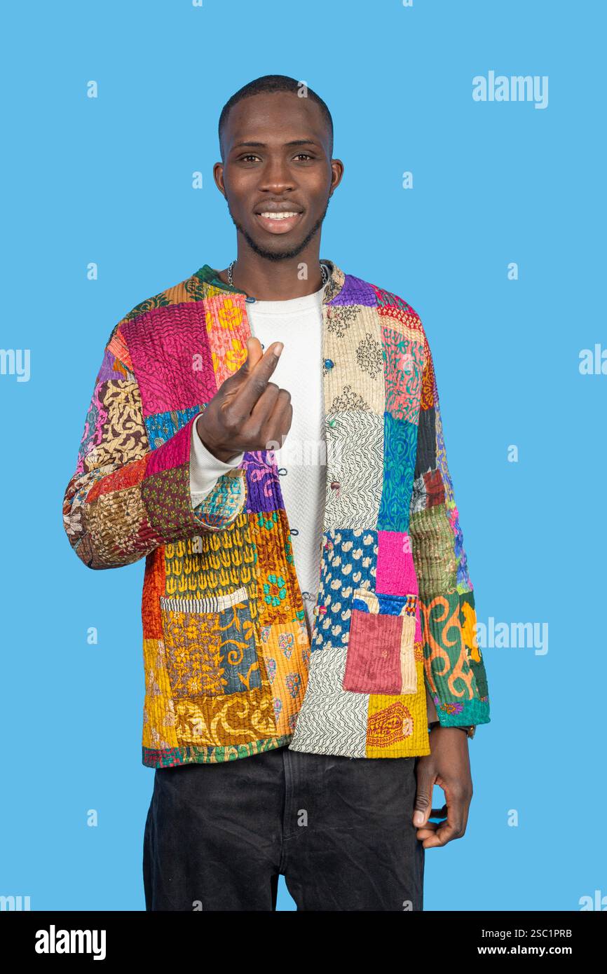 Homme élégant claquant les doigts, portant une veste patchwork colorée sur un fond bleu vif, mettant en valeur la mode et l'individualité Banque D'Images