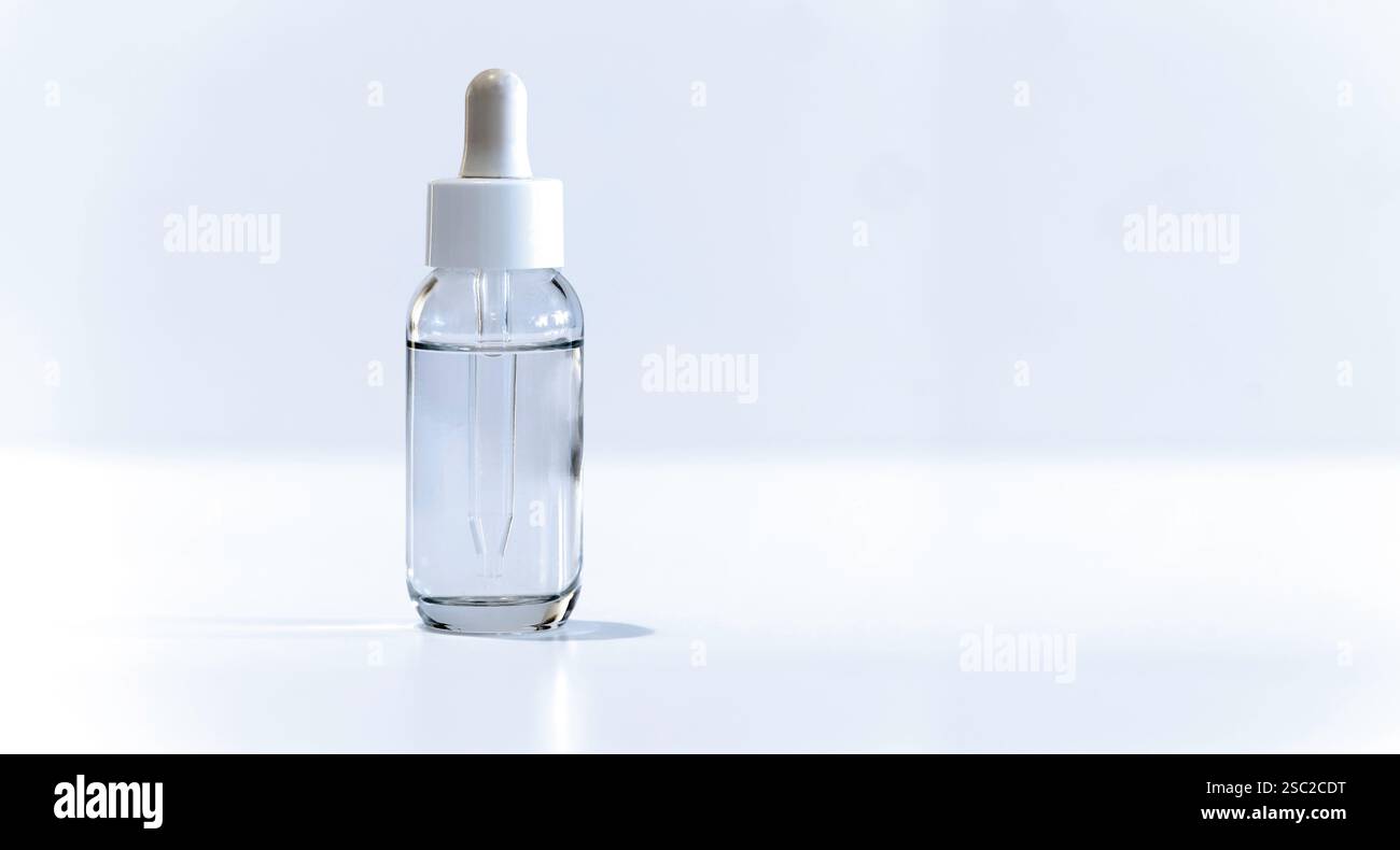 Récipient en verre rempli de liquide clair sur fond blanc. Le capuchon comporte un compte-gouttes pour distribuer le contenu. Banque D'Images