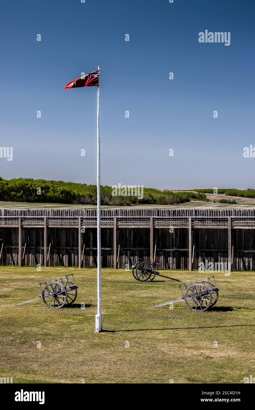 Un mât de drapeau avec un drapeau rouge sur le dessus. Il y a trois vieux chariots dans l'herbe Banque D'Images