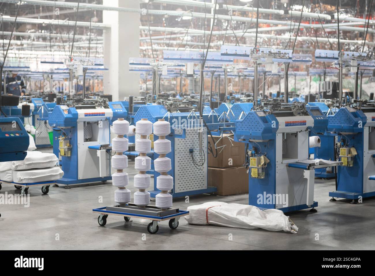 Vue de machines automatisées de fabrication de textiles dans une usine, avec des bobines de fil blanc prêtes pour le traitement. Banque D'Images