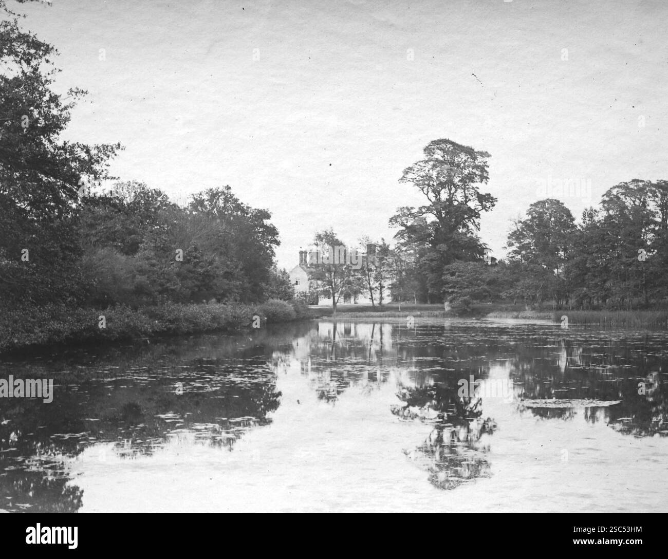 Vue sur la rivière avec des arbres réfléchis et la lointaine Packwood House, un manoir Tudor, Packwood, Warwickshire, Angleterre. C1900s, monochrome : d'une importante collection historique de photographies originales et inattribuées de l'albumen de la fin de l'époque victorienne au début de l'époque édouardienne : une tournée britannique comprenant le Staffordshire, le Warwickshire et le nord du pays de Galles. La qualité des originaux était variable et la plupart étaient autour de 108x165mm. Banque D'Images