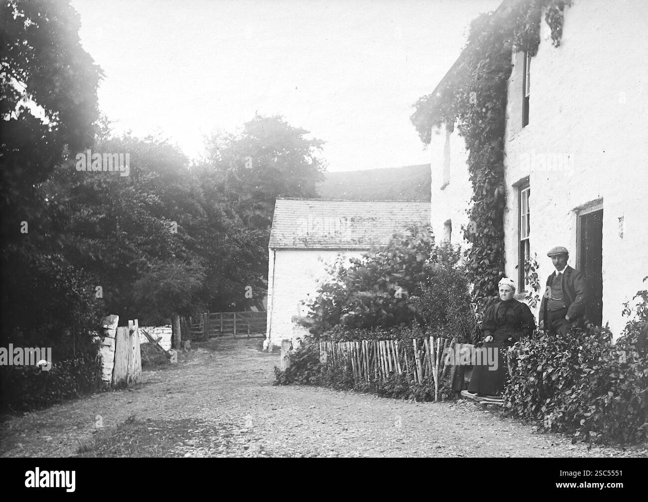 Un homme et une dame devant une maison sur une voie de campagne, Llanilar, Ceredigion, pays de Galles. C1900s, monochrome : d'une importante collection historique de photographies originales et inattribuées de l'albumen de la fin de l'époque victorienne au début de l'époque édouardienne : une tournée britannique comprenant le Staffordshire, le Warwickshire et le nord du pays de Galles. La qualité des originaux était variable et la plupart étaient autour de 108x165mm. Banque D'Images
