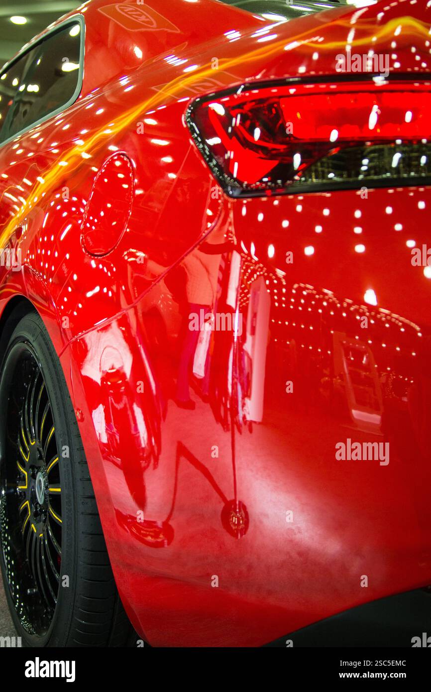 Une voiture rouge très polie et éclatante lors d'un salon ou d'une exposition automobile est au centre des préoccupations. La peinture de la voiture est brillante, reflétant l'éclairage intérieur. Banque D'Images