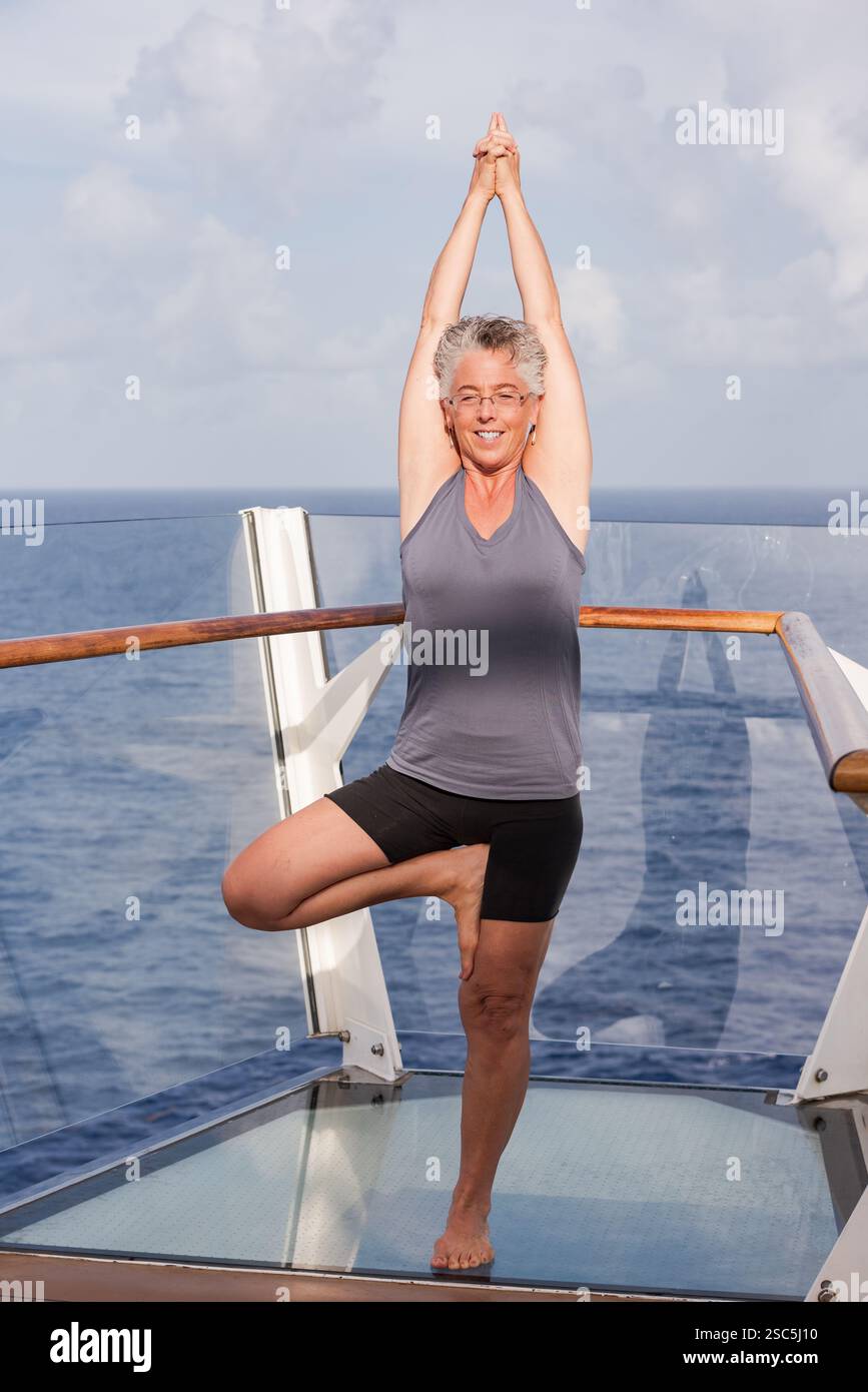 Forte, en forme, femme mature frappant l'arbre de yoga strenuos pose à l'extérieur sur le pont du navire. Banque D'Images