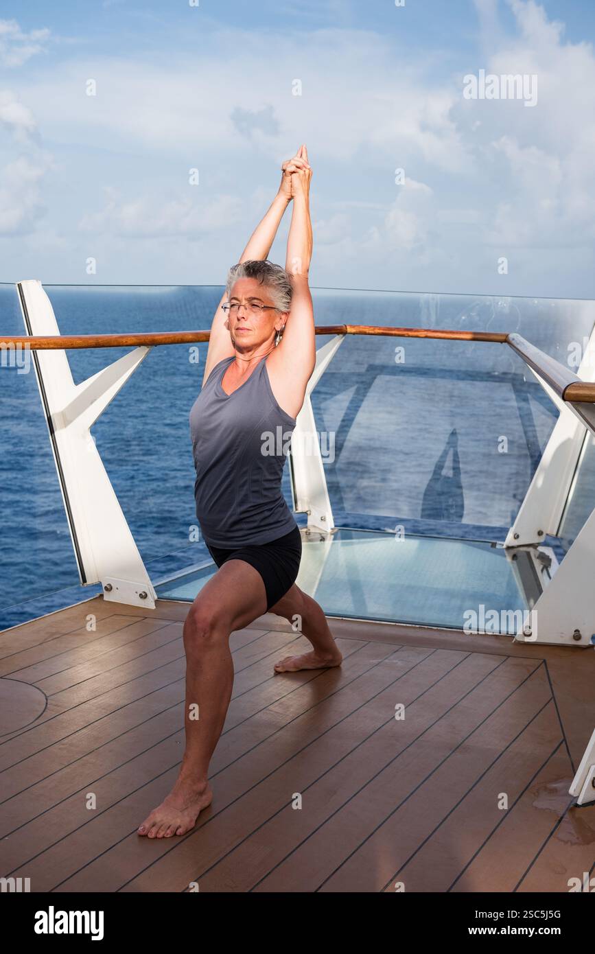 Forte, en forme, femme mature frappant strenuos yoga pose à l'extérieur sur le pont du navire. Banque D'Images