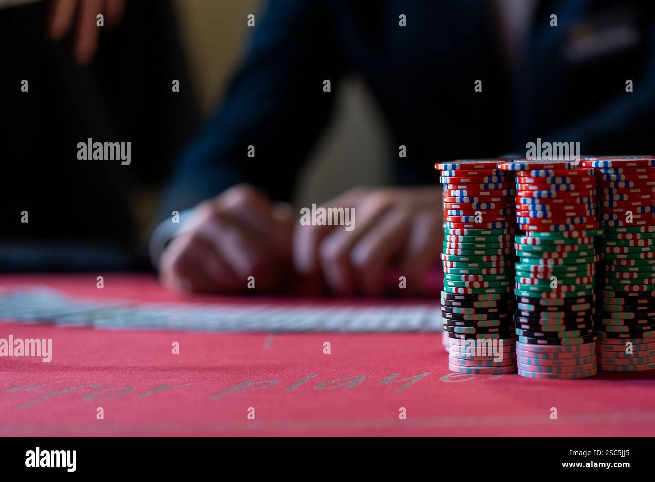 Piles de jetons de poker sur une table de casino avec un croupier en arrière-plan, symbolisant le jeu à enjeux élevés, la chance, et le frisson des Paris. Banque D'Images