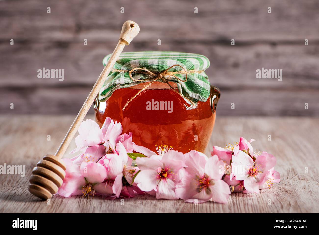 Pot de miel de fleur recouvert d'un chiffon, à côté d'une cuillère à miel ou d'une benne et fleurs d'amande. Banque D'Images