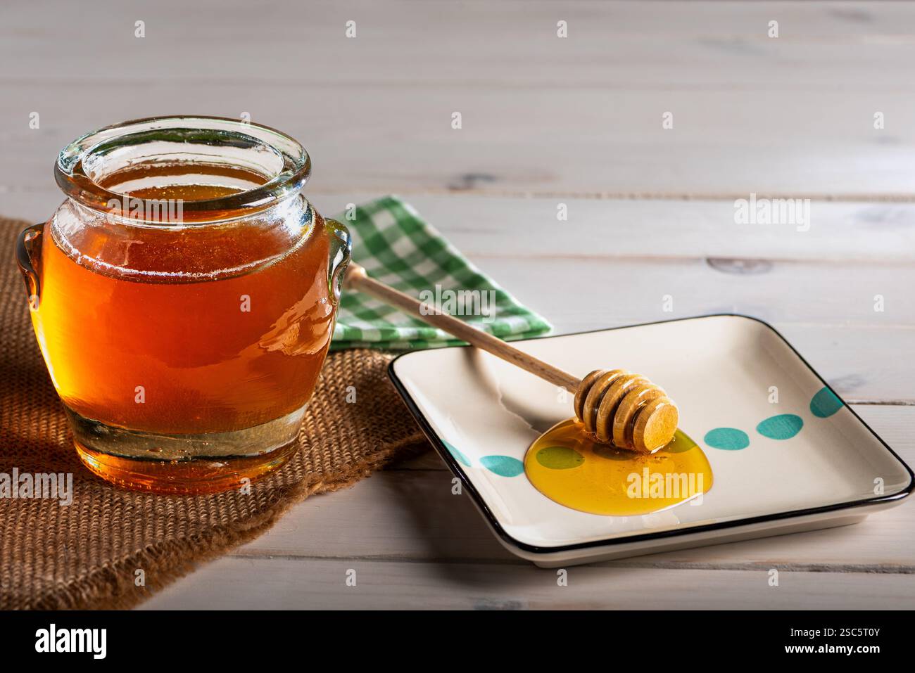 Trempette de miel sur une petite assiette avec du miel, à côté d'un pot rempli de miel de fleur, sur une table en bois blanc. Banque D'Images