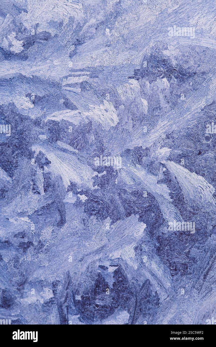 Gros plan des motifs givrés sur le verre, créés par des températures glaciales. Cristaux de glace abstraits et formations de gel ressemblant à des paysages hivernaux Banque D'Images