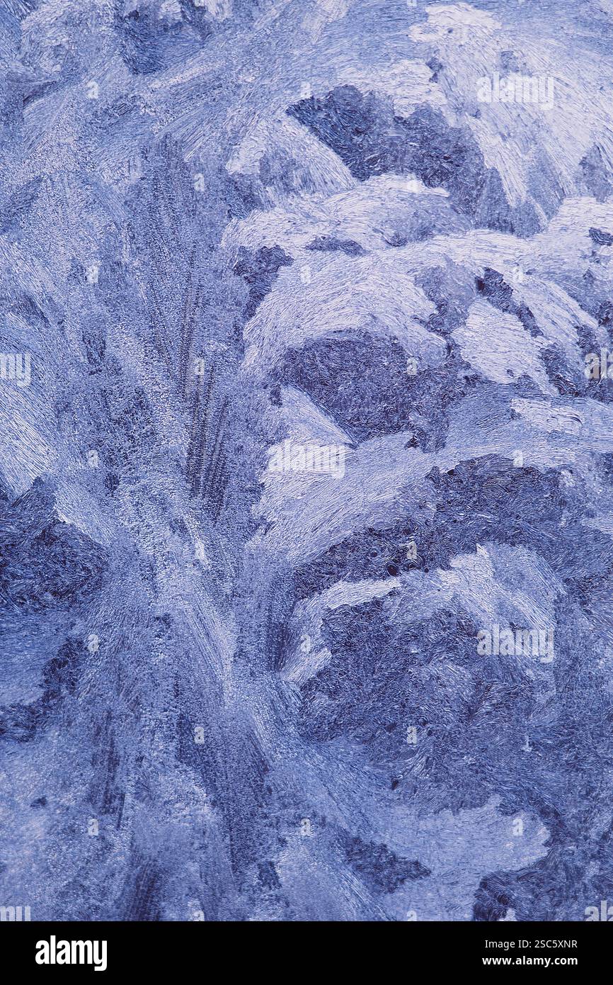 Gros plan des motifs givrés sur le verre, créés par des températures glaciales. Cristaux de glace abstraits et formations de gel ressemblant à un paysage hivernal Banque D'Images