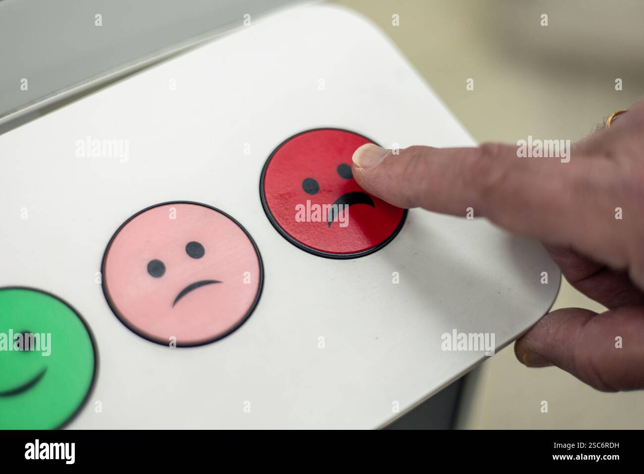 Main appuyant sur un bouton rouge avec une émoticône triste pour les commentaires négatifs, exprimant l'insatisfaction avec un service ou un produit, avec d'autres émoticônes dans le th Banque D'Images