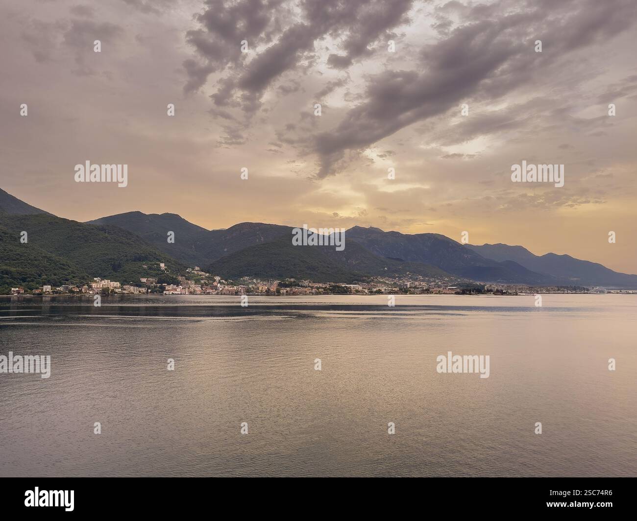 Baie de Kotor, Monténégro - 2 juillet 2024 : lever du soleil sur la ville de Tivat à l'extrémité est de la baie inférieure montre un ciel jaune sous des nuages gris. Montagnes sombres et Banque D'Images