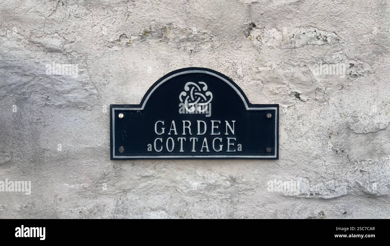Nom de la maison en métal Garden Cottage attaché à un mur de pierre peint blanc sur une maison - Image de stock capturée avec un smartphone