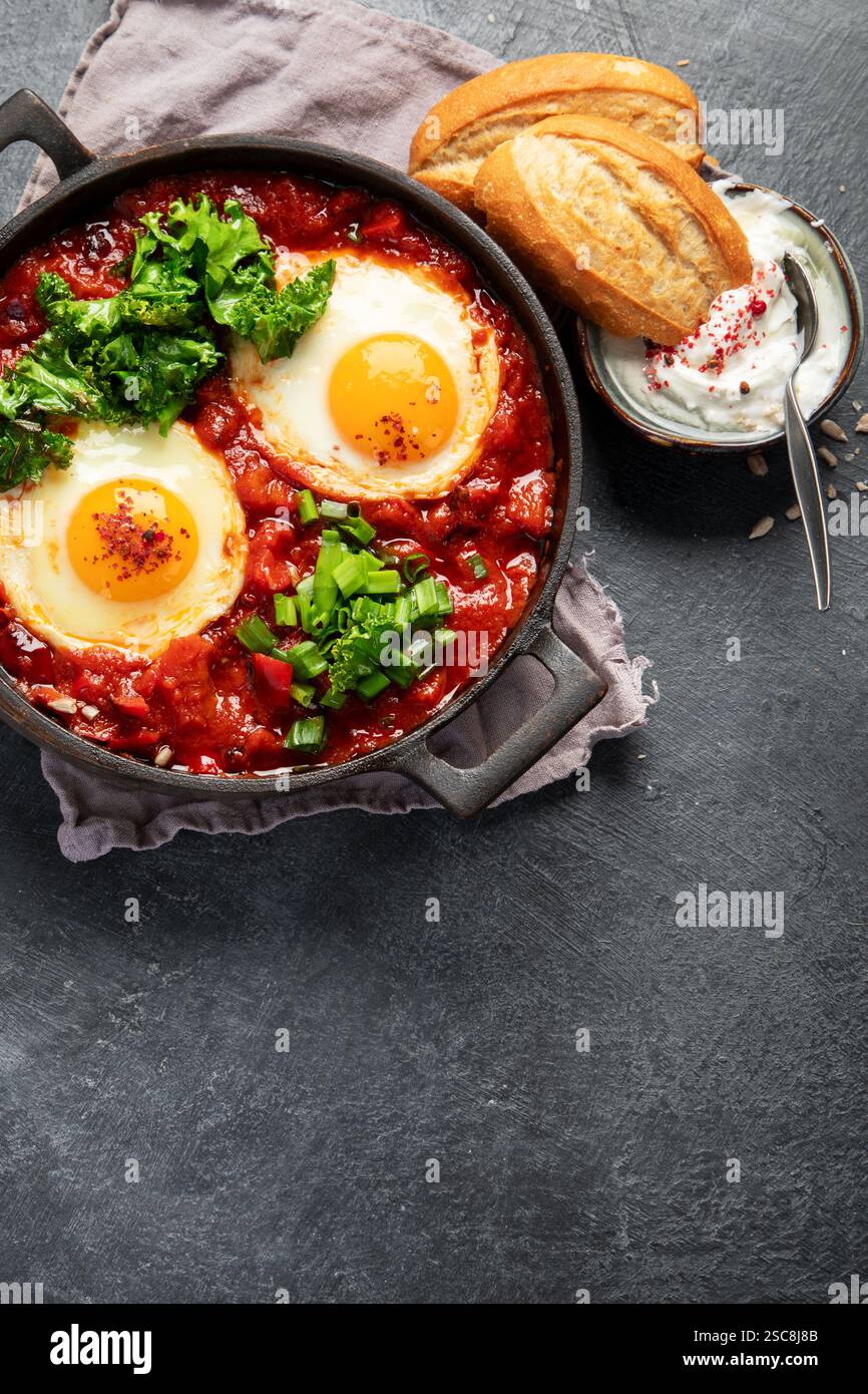 Oeufs Shakshuka dans une casserole avec du pain sur un fond sombre. Oeufs pochés dans une sauce épicée au poivre tomate. Œufs brouillés juifs traditionnels. Vue de dessus. Co Banque D'Images