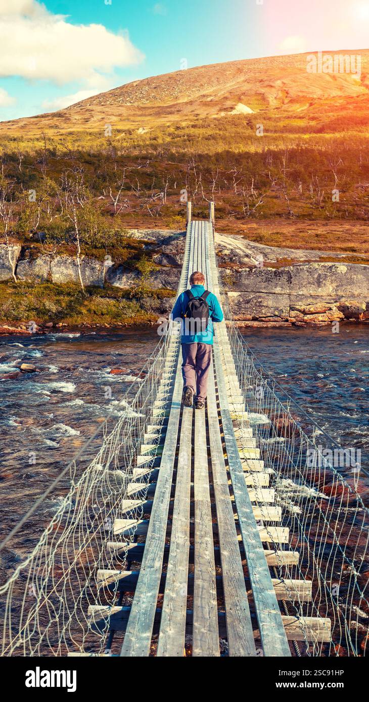 Un homme traverse une rivière de montagne sur un pont suspendu. Bannière verticale Banque D'Images