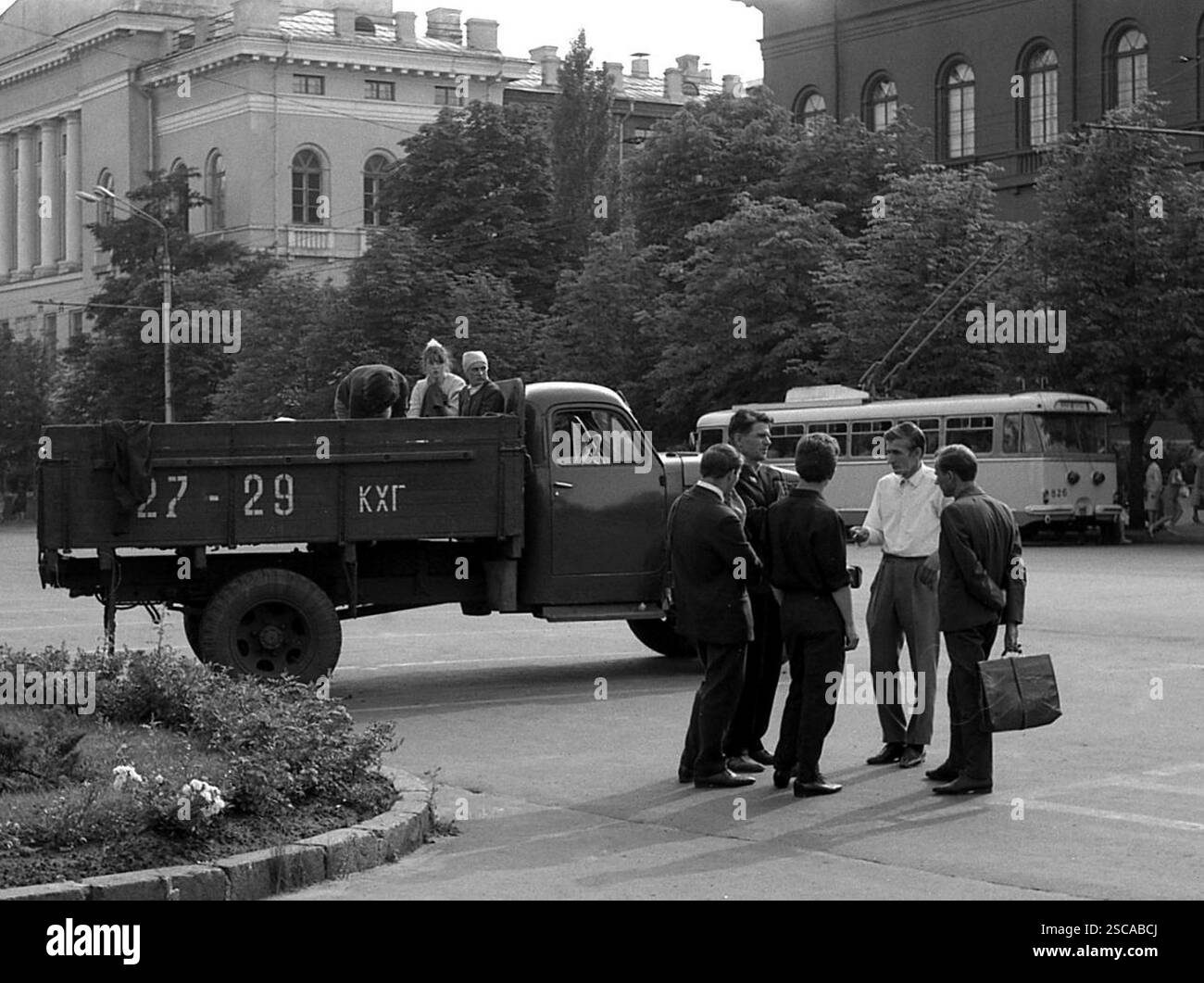 Un groupe d'hommes se tiennent ensemble par un camion et parlent. Deux femmes et un homme s'assoient ou se tiennent sur la zone de chargement de la voiture. En arrière-plan, vous pouvez voir un bus de chariot. [traduction automatique] Banque D'Images