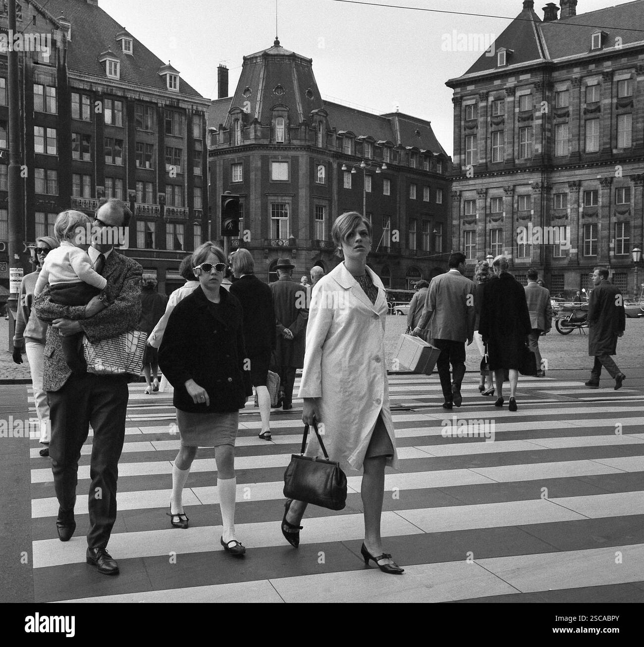 Père avec l'enfant sur ses bras, fille avec des mi-bas et des lunettes de soleil et un manteau, sac à main femme avec des talons hauts et de traverser une rue. Banque D'Images
