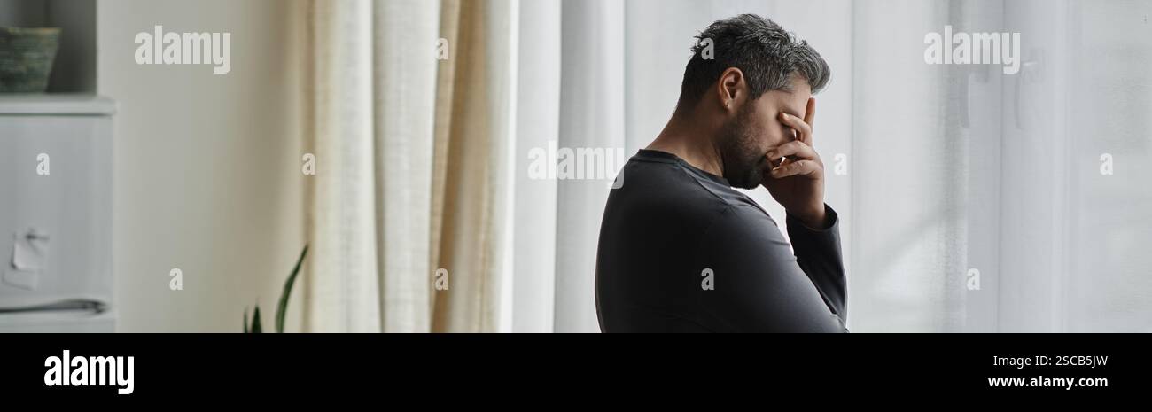 Un bel homme apparaît profondément dans la pensée alors qu'il repose son front sur sa main près de la fenêtre. Banque D'Images