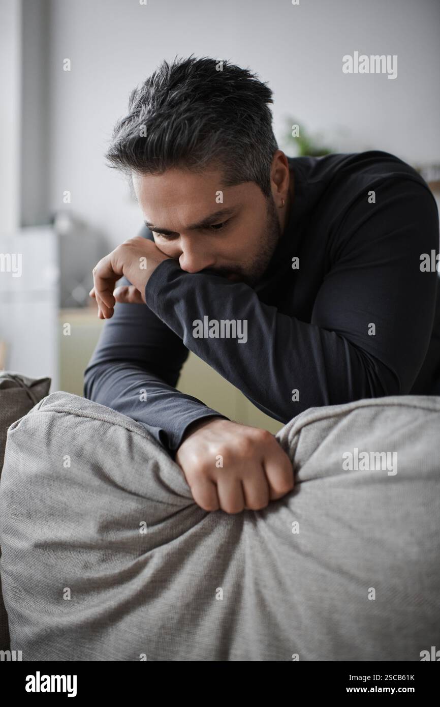 Un homme réfléchi se penche sur un canapé, profondément dans la contemplation, entouré d'un environnement calme et confortable. Banque D'Images