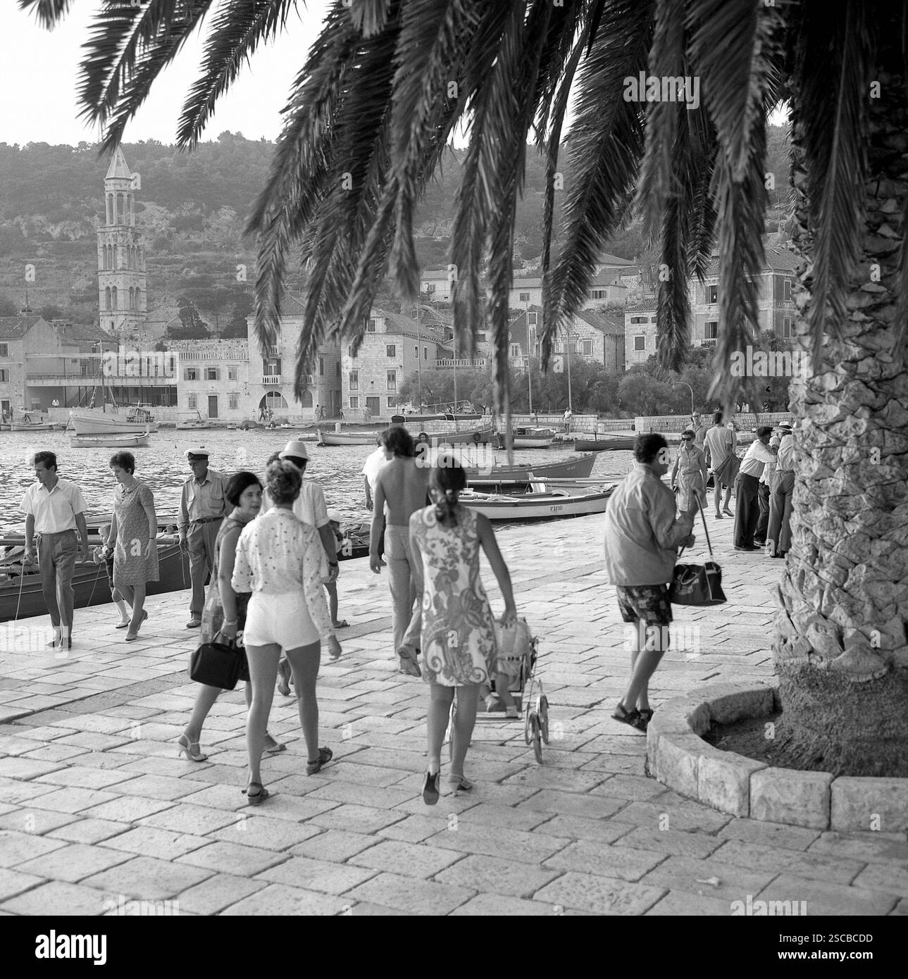 'Homme avec chapeau de capitaine', une femme portant une robe avec buggy et marcheurs au port de Hvar.' Banque D'Images