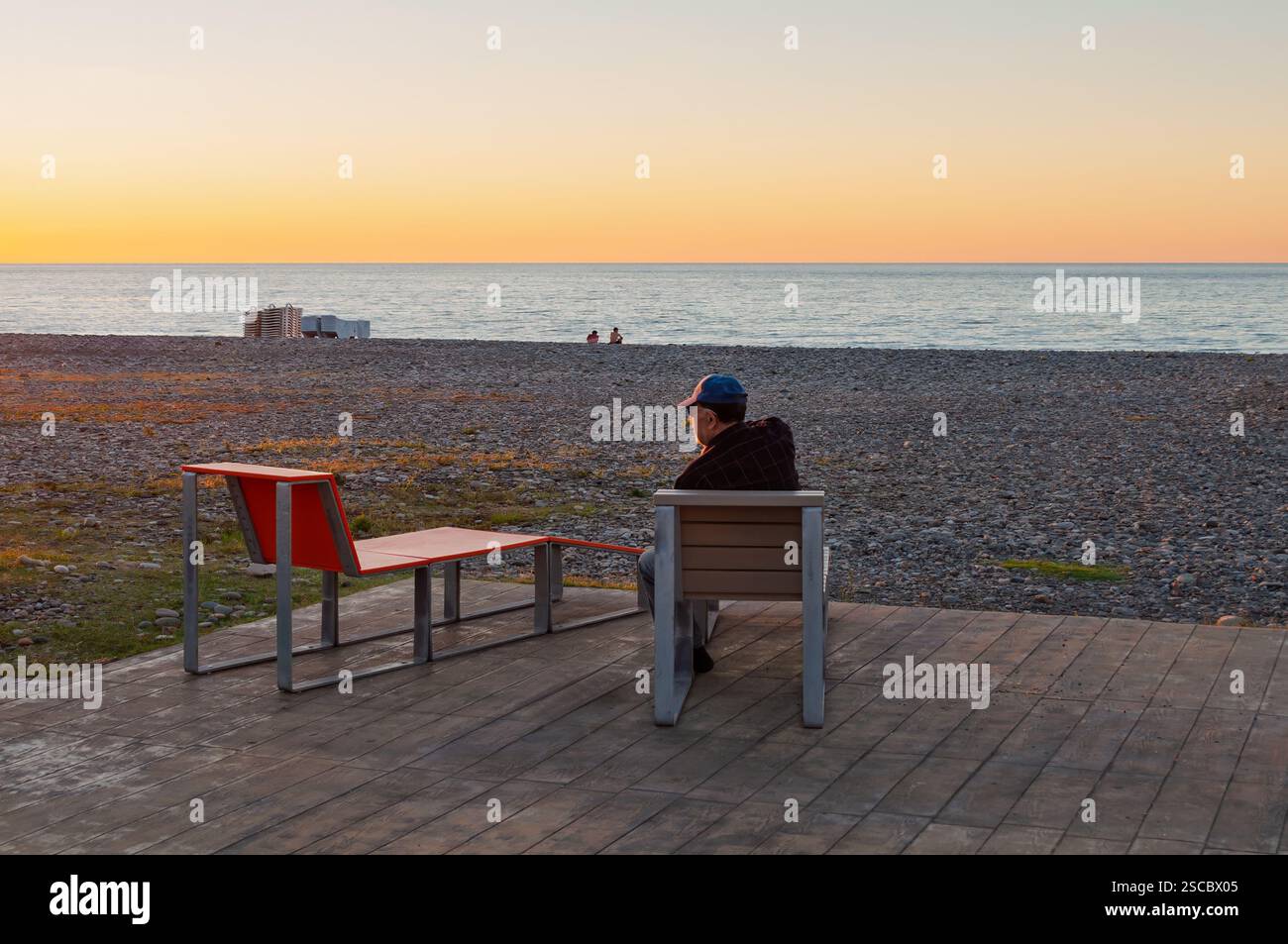 Batumi, Géorgie. 23 décembre 2013. Homme solitaire se reflète au bord de la mer pendant le coucher du soleil, chaise vide symbolisant l'absence ou la perte. Banque D'Images