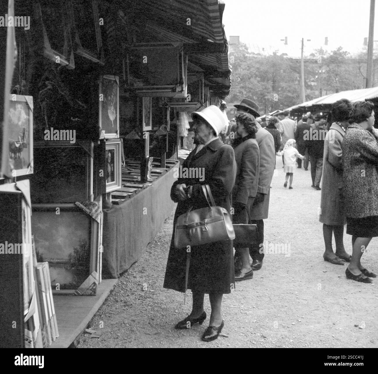 Une vieille femme avec un sac à main regardant des peintures à un étalage au Kirchweih-Dult à au à Munich. [traduction automatique] Banque D'Images