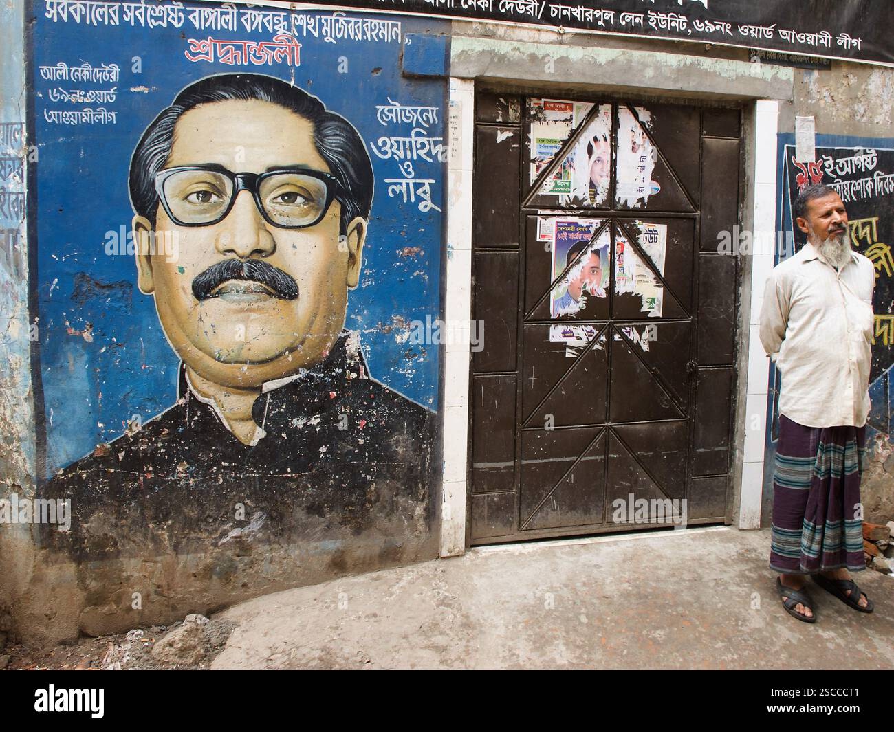 Murale du cheikh Mujibur Rahman sur un mur altéré à Dacca, avec un homme dans un poumon debout à côté, observant la rue. Banque D'Images