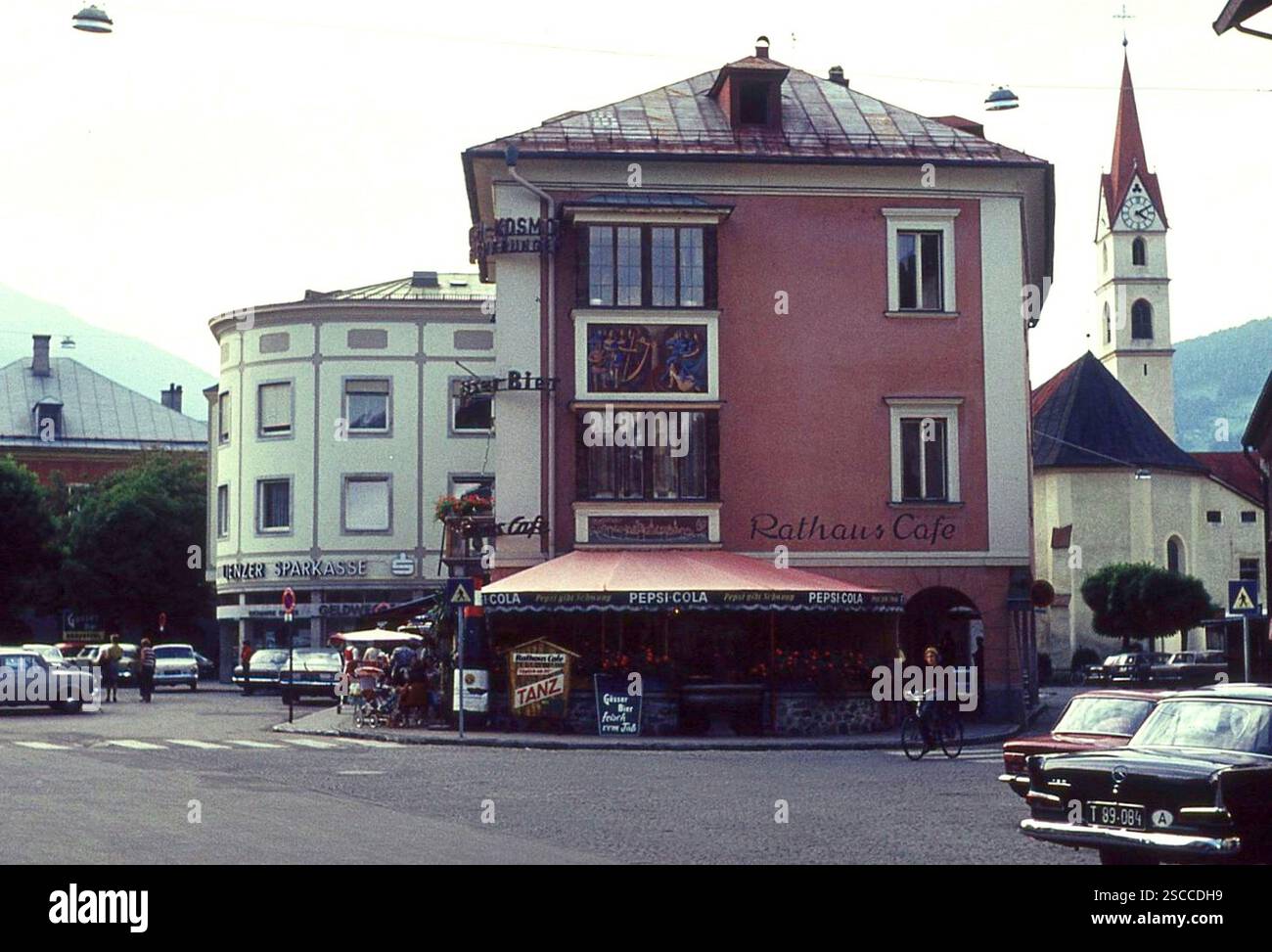 Vue sur la Rathaussplatz dans le Tyrol de l'est. Le Rathaus Cafe annonce la danse, la bière Gösser fraîche du baril et Pepsi-Cola (Pepsi donne de l'élan). En arrière-plan sur la gauche se trouve la Linzer Sparkasse, sur la droite vous pouvez voir la tour de l'église. Les voitures Mercedes sont stationnées sur la place. [traduction automatique] Banque D'Images